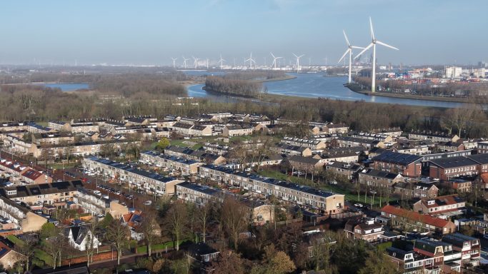 Luchtbeeld van een stad met water, windmolens en woningen omringd door natuur.